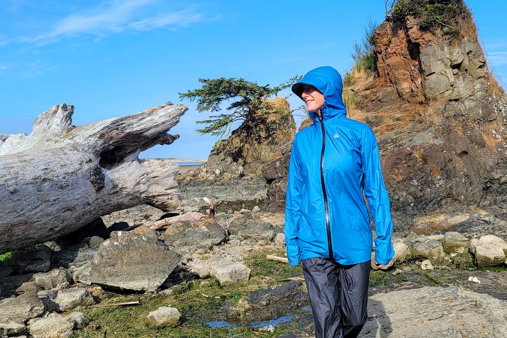 A hiker wearing the Zpacks Vertice Rain Jacket with the hood up on a coastal hike